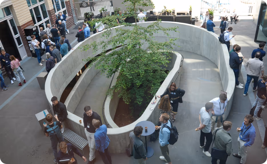 Overhead view of a modern indoor courtyard with a spiral concrete planter containing a tree, surrounded by people socializing and standing in groups.